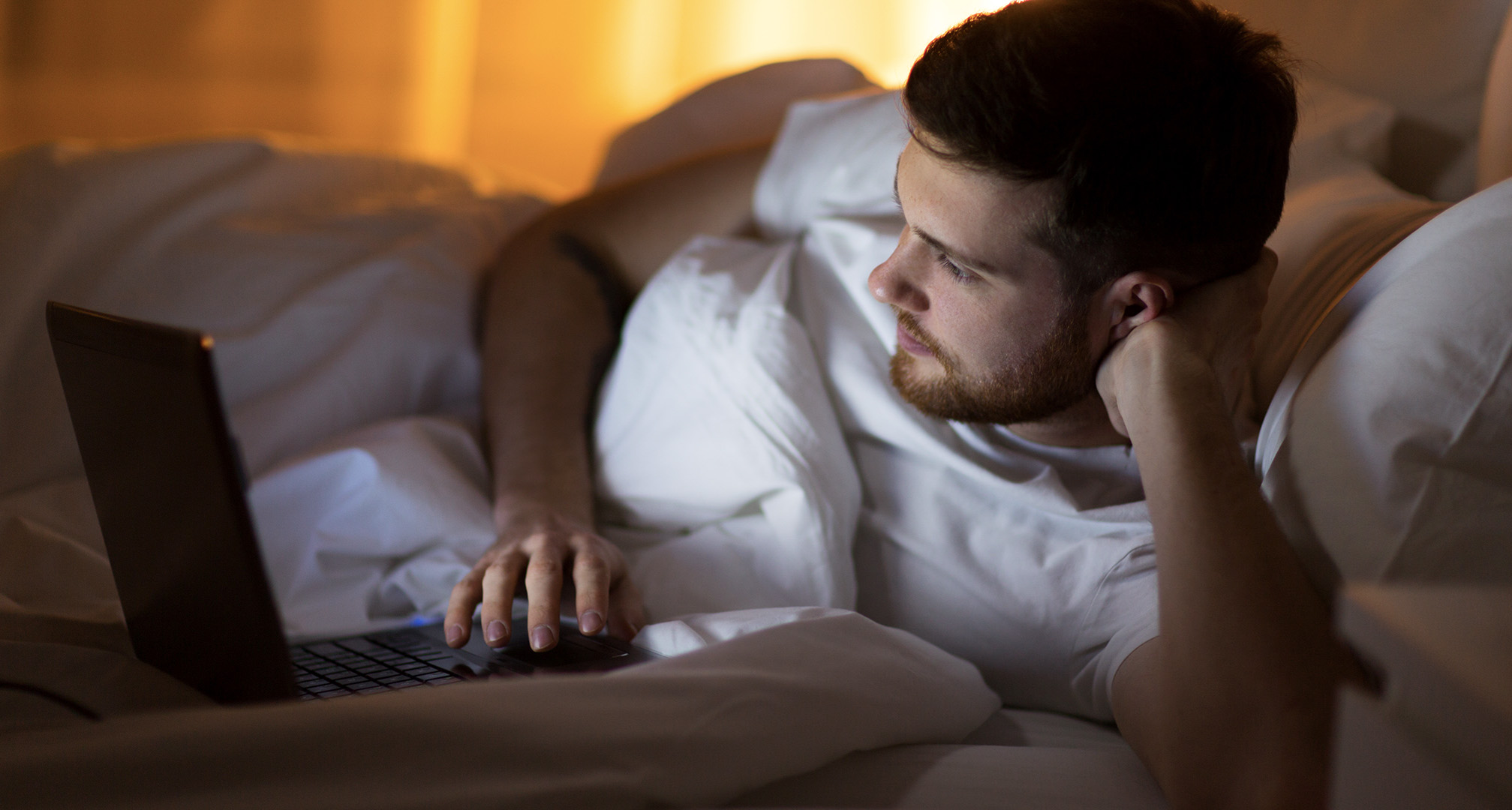 Person, die nachts vom Bett aus einen Laptop benutzt