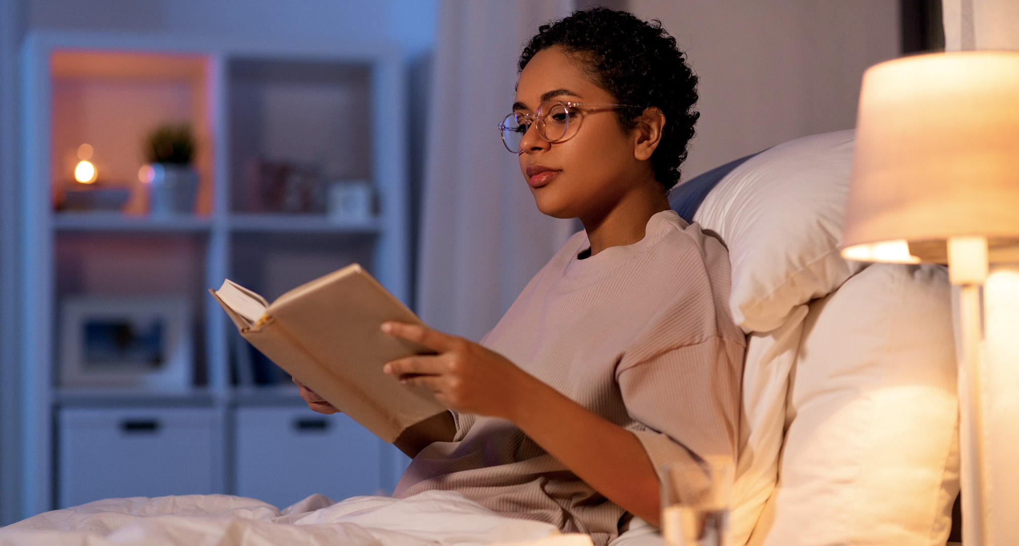 Person mit Brille, die in einem schwach beleuchteten Raum ein Buch liest